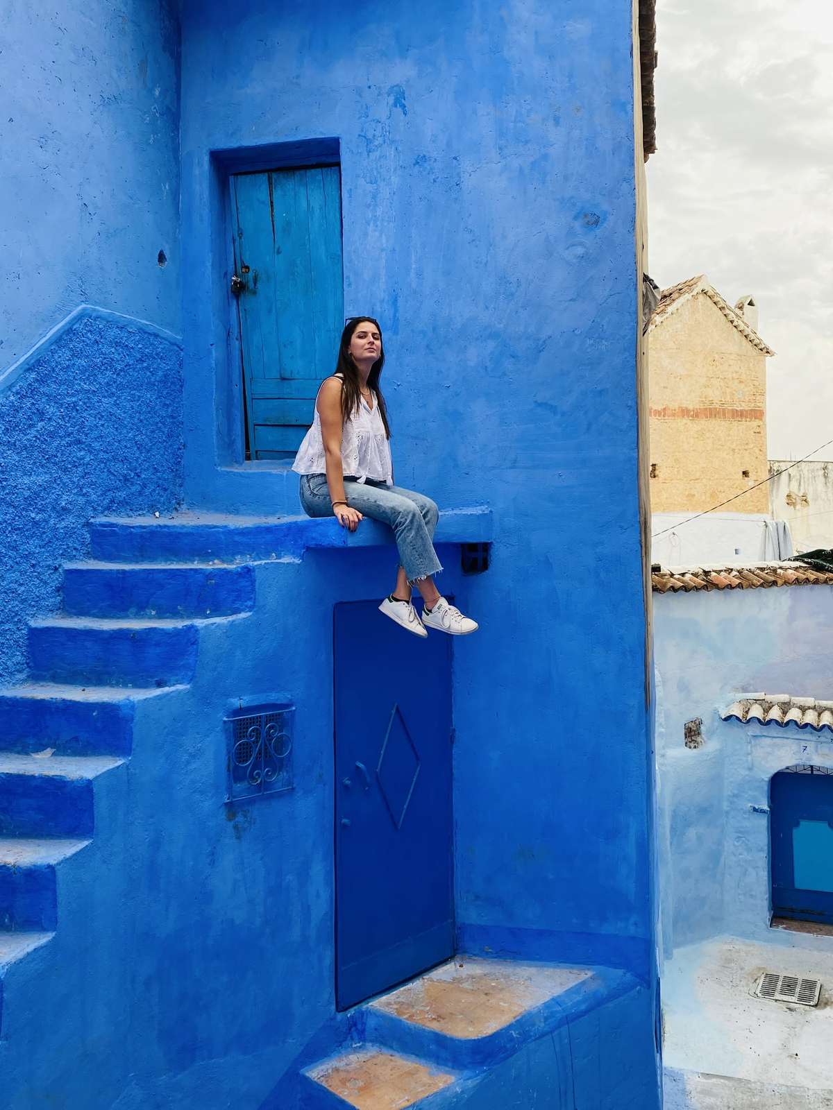 Viajera sentada sobre una puerta azul en Chefchaouen