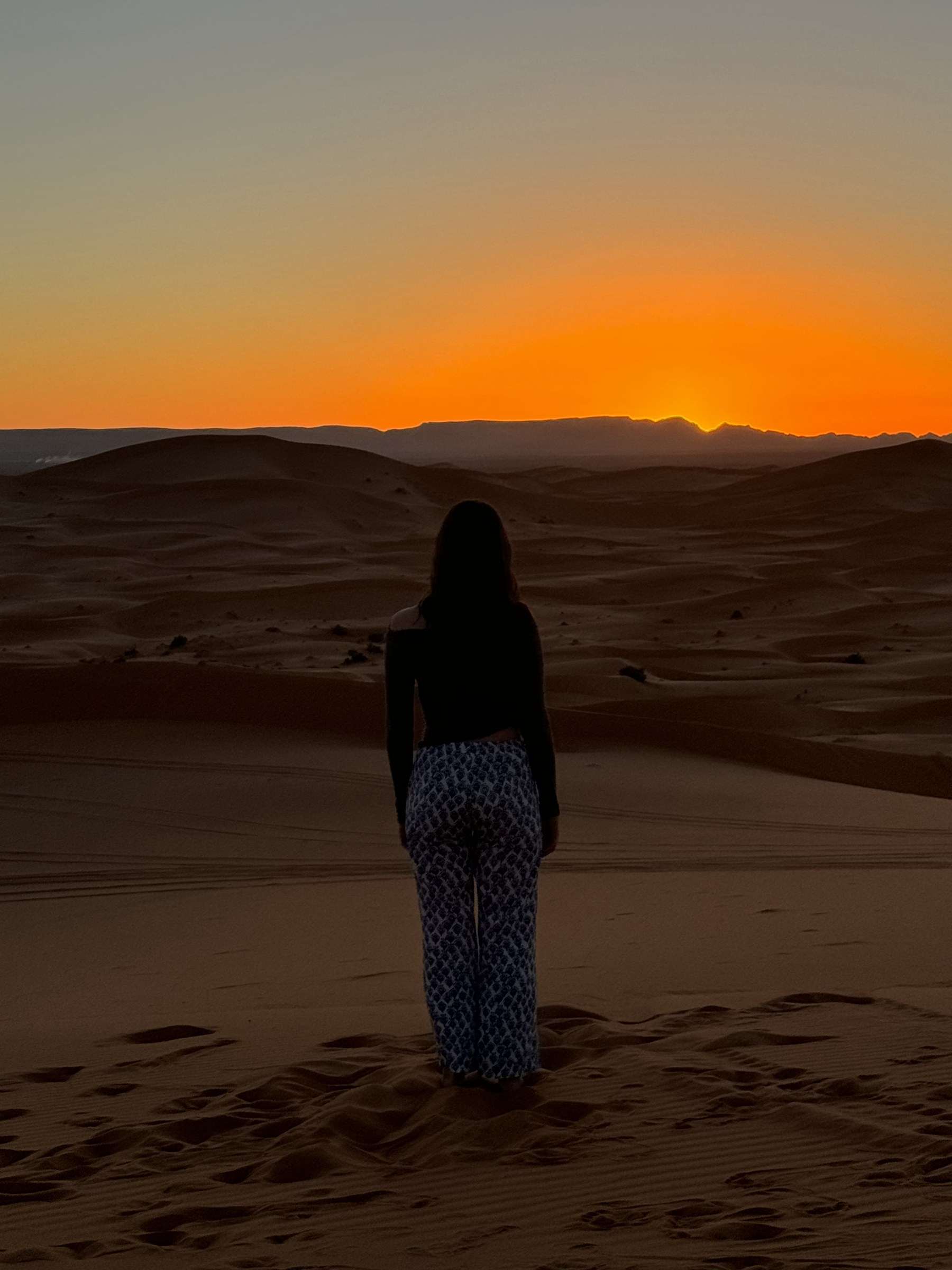 Silueta de viajera contemplando el atardecer sobre las dunas de Merzouga